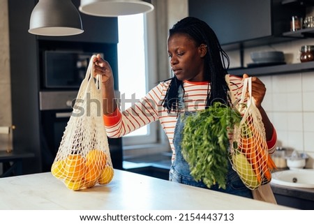 African woman unloading fresh vegetables from her reusable shopping bag at home.
