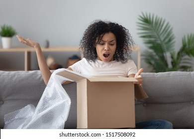 African woman unpack box feels angry received see broken ordered goods gesticulates with hands negative face expressions, concept of damaged or wrong parcel, dissatisfied client, complaints and claims
