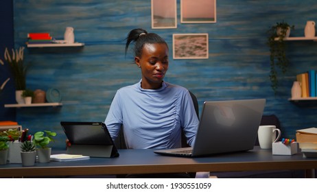 African woman using laptop and tablet in same time in office living room working overtime. Busy focused black employee using modern technology network wireless overworking writing, searching.