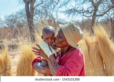 African Woman In The Village Carrying Her Child In The Back, Wrapped In A Blanket