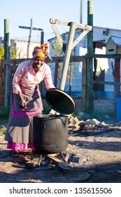 african woman watching over her dinner in big black pot outside on fire