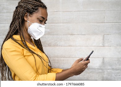 African woman wearing face medical mask using mobile smartphone - Young girl with braids having fun with phone during corona virus outbreak - Health care people and technology concept  