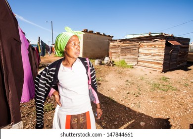 An African Woman Wearing A Lime Green Bandanna Standing With Her Hand On Her Hip In Attitude Next To Her Washing Line