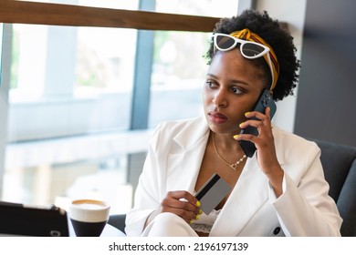 African Woman In A White Suit Gives A Talk On The Phone And Reports Her Bank Details Holding A Bank Card. Bank Or Credit Card. Concept: Purchase Credit Mortgage 