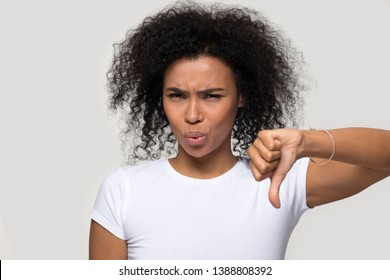 African woman in white t-shirt looking at camera contemptuously showing thumb down gesture symbol of negative feedback, bad quality evaluation and dislike, disagreement not recommend rejection concept