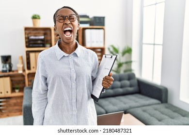 African woman working at psychology clinic angry and mad screaming frustrated and furious, shouting with anger. rage and aggressive concept.  - Shutterstock ID 2180487321