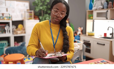 African woman working as teacher writing on clipboard at kindergarten