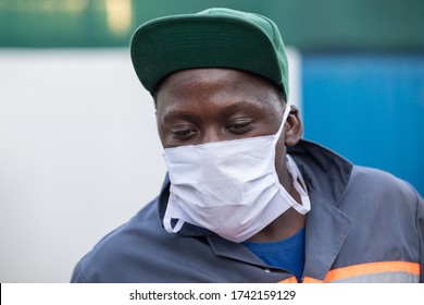 African Worker  Wearing A Mask, Outdoors View, Exiting A Metallic Door At A Warehouse 