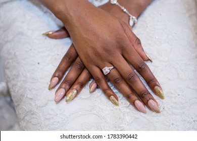 African young bride's elegant hands, new beautiful golden diamond engagement ring, long oval nails, beige and gold manicure, silver bracelet on the wrist, white lace wedding dress on the background - Shutterstock ID 1783390442
