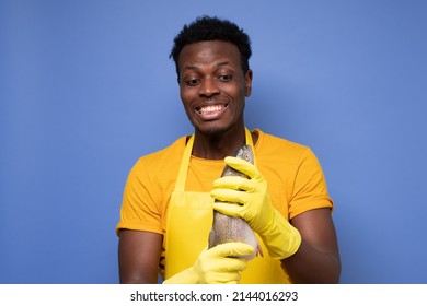 African Young Cook Holding A Fresh Fish On A Purple Background. Studio Shot