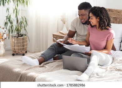 African Young Couple Checking Family Budget On Weekend, Holding Papers And Using Laptop At Bedroom, Free Space