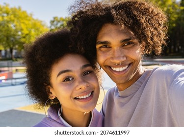 African young couple dating outdoors, colored and modern urban background - Multiethnic people with stylish and cool urban clothes bonding outdoors and taking pov selfie