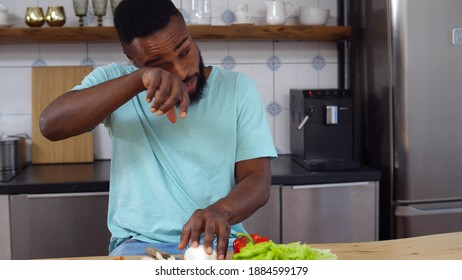 African Young Man Crying Chopping Onion For Vegetable Salad In Kitchen. Portrait Of Afro-american Guy Having Tears Cutting Onion For Vegetarian Dinner At Home