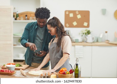 African Young Man Showing Recipe In His Mobile Phone To Woman Who Making Dough For Pizza In The Kitchen At Home