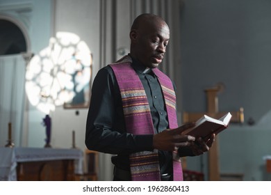 African young priest reading the Bible during mass while standing near the altar in church
