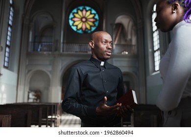 African young priest talking to woman and discussing the parts of Bible standing in the church