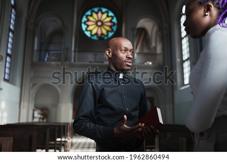 African young priest talking to woman and discussing the parts of Bible standing in the church
