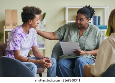 African young psychologist talking to teenage boy during therapy session at classroom - Powered by Shutterstock