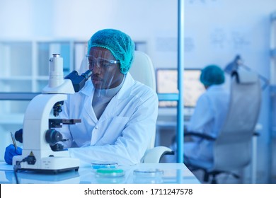 African young scientist sitting at his workplace and working with microscope during scientific experiment at office - Powered by Shutterstock - Get 15% off with code: PIKWIZARD15