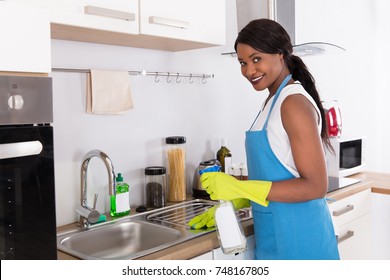 African Young Woman Cleaning Kitchen Sink With Spray Bottle In Kitchen