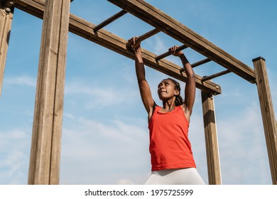 African young woman climbing monkey bars in military training boot camp outdoors at city park - Focus on girl face - Powered by Shutterstock