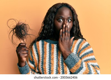 African Young Woman Holding Comb Loosing Hair Covering Mouth With Hand, Shocked And Afraid For Mistake. Surprised Expression 