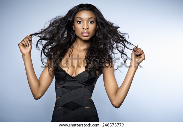 African young woman with long hair\
wearing small bandage black dress on blue background.\
