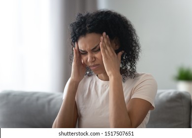 African young woman sit on couch frown face expressions touches temples reduces sharp severe migraine or headache feeling discomfort unpleasant sensations caused by weather?changes or hangover concept - Shutterstock ID 1517507651