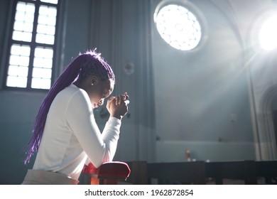 African young woman sitting in front of the altar in the church and praying