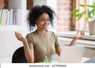 African young woman sitting at table opposite laptop in workplace meditating doing yoga exercise smiling feels good. Take a break, inner balance and harmony, stress relief no negative emotions concept - Powered by Shutterstock