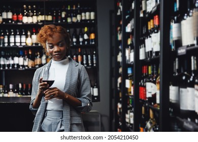 African Young Woman Sommelier Holds Glass With Red Wine In Restaurant, Tests Aroma And Color.