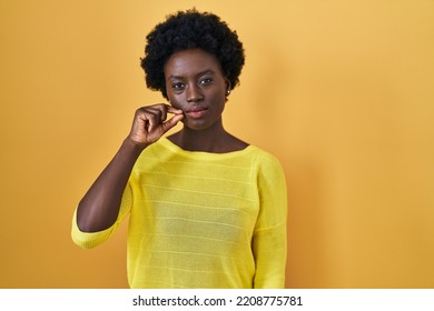 African Young Woman Standing Over Yellow Studio Mouth And Lips Shut As Zip With Fingers. Secret And Silent, Taboo Talking 