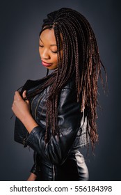 African Young Woman Studio Portrait Wearing Black Leather Jacket With Braids Against Dark Background.