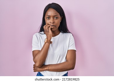 African young woman wearing casual white t shirt looking stressed and nervous with hands on mouth biting nails. anxiety problem. 