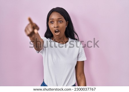 African young woman wearing casual white t shirt pointing with finger surprised ahead, open mouth amazed expression, something on the front 