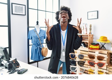 African young woman working as manager at retail boutique crazy and mad shouting and yelling with aggressive expression and arms raised. frustration concept. 