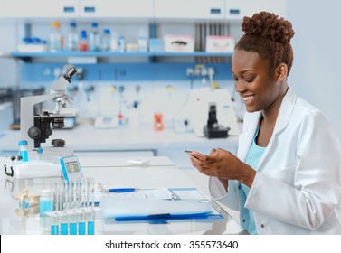 African-american Biologist In The Lab Texting Someone On Her Mobile With A Smile