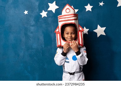 African-American boy in an astronaut costume stands against a background of a blue wall with a starry sky - Powered by Shutterstock