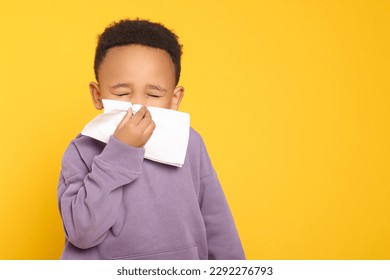 African-American boy blowing nose in tissue on yellow background, space for text. Cold symptoms - Powered by Shutterstock