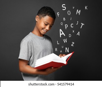African-American boy with book and alphabet letters on dark background. Speech therapy concept