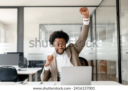 The African-American businessman is captured in a moment of victory, his arm thrust upwards in elation, laptop in front. This shot conveys the exuberance of personal and professional accomplishments