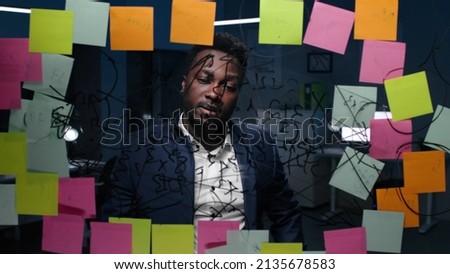 African-American businessman look at glassboard with notes in dark office