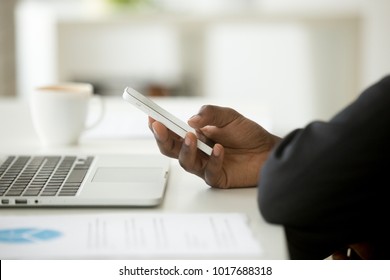 African-american businessman in suit using mobile phone in office, black man holding smartphone at workplace with laptop computer, corporate devices and apps for business concept, close up side view