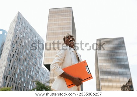 an African-American businesswoman, laughing happily, holding an orange folder in her hands.