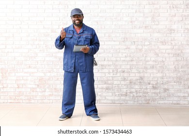 African-American car mechanic with tablet computer showing thumb-up near brick wall - Powered by Shutterstock