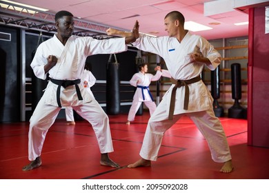 African-american and caucasian men in kimono and belts fighting against each other during karate training in gym.