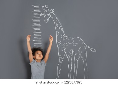 African-American Child Measuring Height Near Chalk Giraffe Drawing On Grey Background