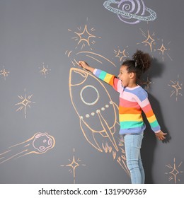 African-American Child Playing With Chalk Rocket Drawing On Grey Background