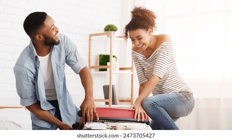 African-american couple trying to close suitcase, preparing for honeymoon - Powered by Shutterstock