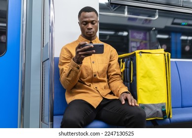 An African-American courier rides in a subway car and watches a TV series on his phone while he goes to pick up an order